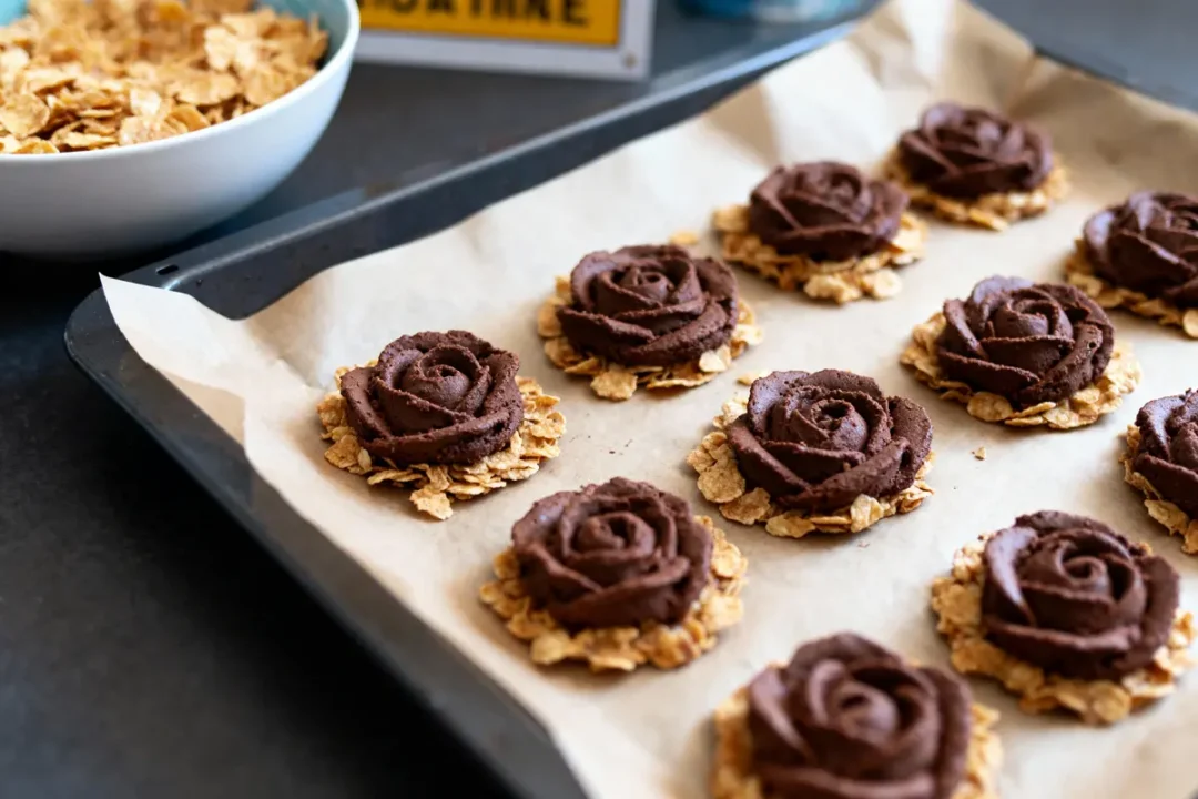 Biscuits au chocolat en forme de roses sur plaque de cuisson, accompagnés d'un bol de céréales.