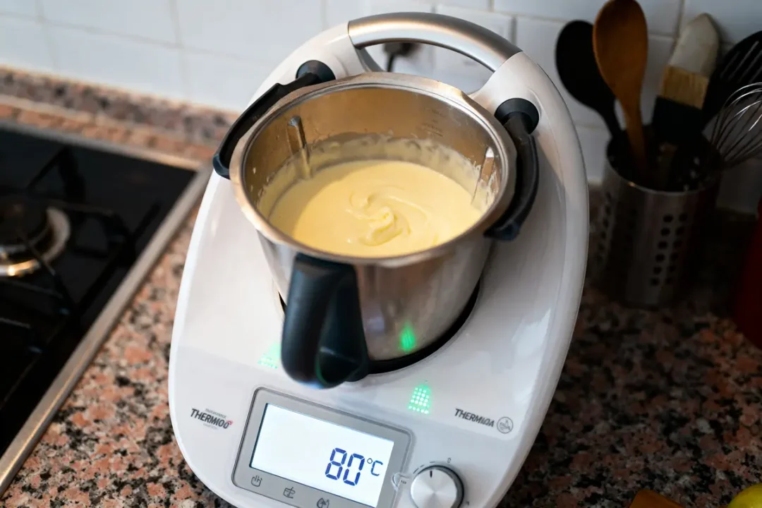 Thermomix préparant une sauce à 80°C dans une cuisine moderne avec ustensiles en arrière-plan.