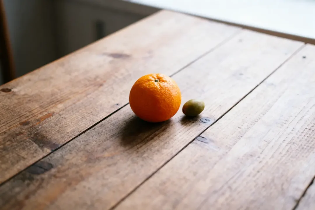 Orange et olive sur une table en bois, éclairage naturel venant d'une fenêtre.