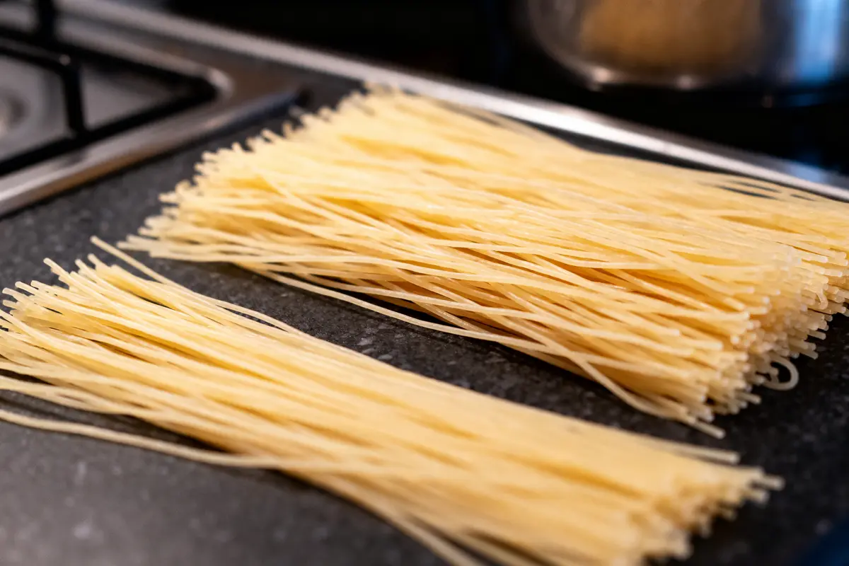 Deux piles de pâtes spaghetti non cuites sur un plan de travail, proche d'une cuisinière.