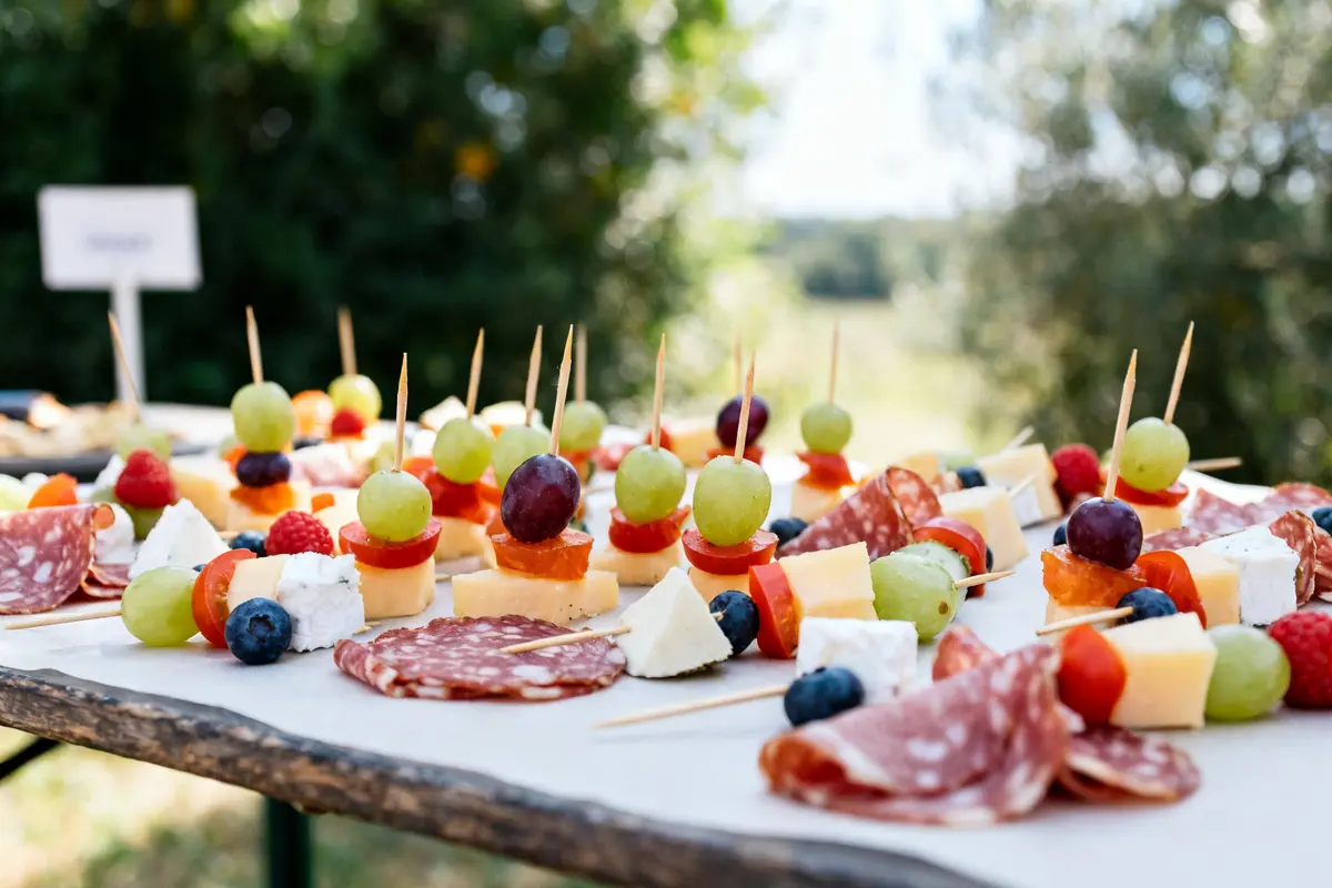 Brochettes apéro froides avec fromage, tomates, raisins sur table de pique-nique extérieure.