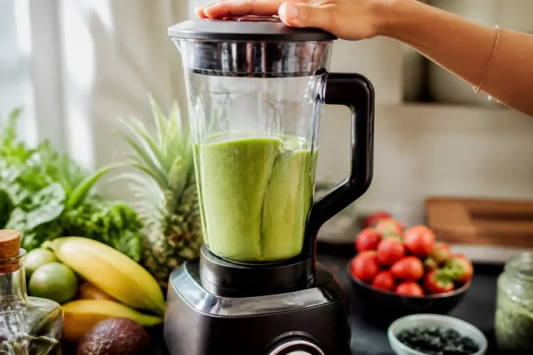 Main utilisant un mixeur sur maviehealthy.com avec fruits et légumes pour smoothie vert